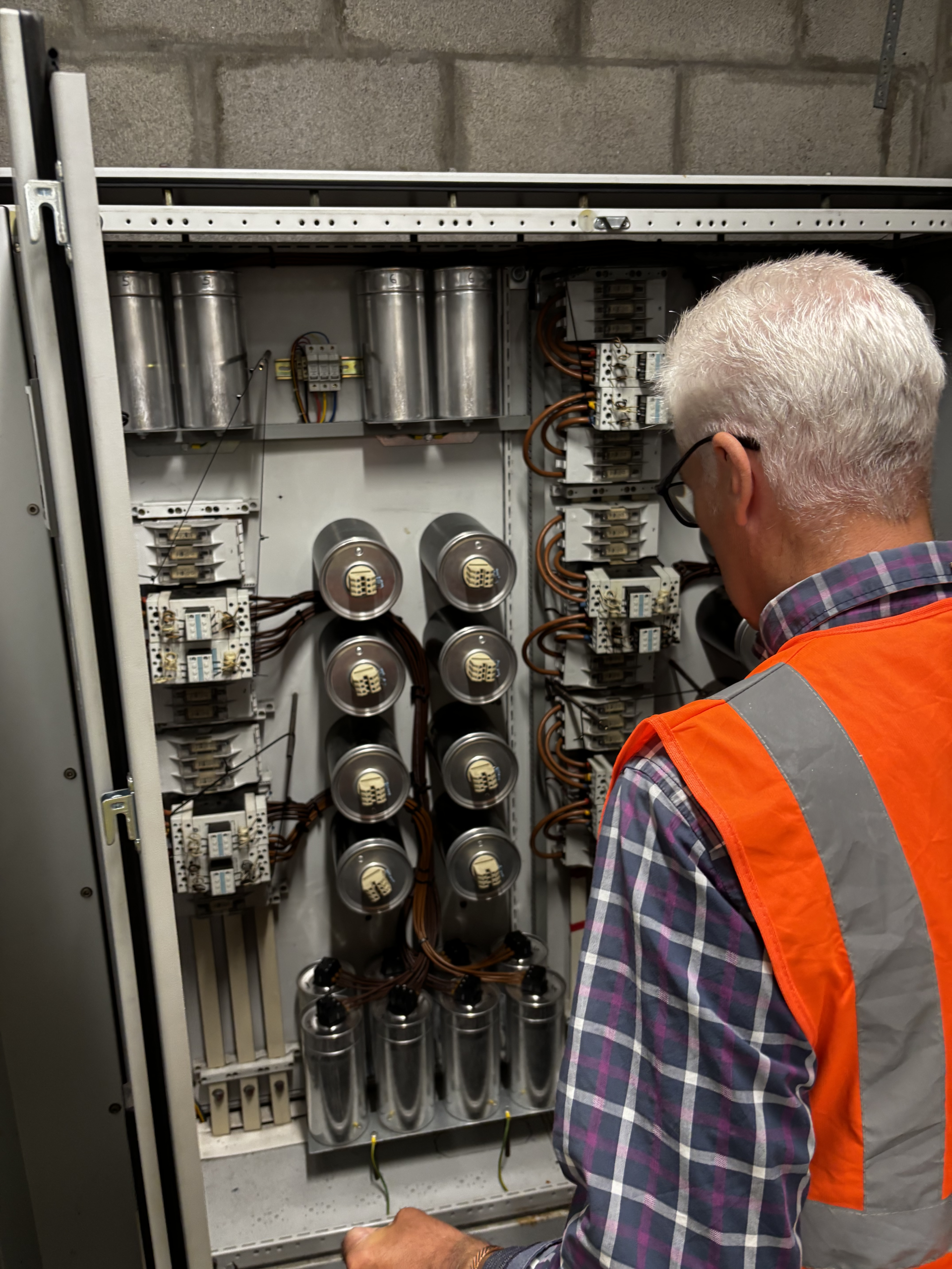 Engineer performing maintenance on a power factor correction unit in a commercial facility